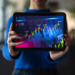 Pessoa segurando um tablet exibindo gráficos de ações em alta, representando o potencial de valorização do mercado em 2026.