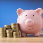 Cofrinho rosa ao lado de moedas simbolizando como investir pouco por mês e construir patrimônio com R$ 200.